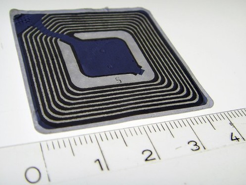 An RFID chip measured against a ruler; one of these can be thrown into a baggage tag (Source: WikiMedia Commons)