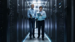 In Data Center Two IT Engineers Walking Through Rows of Server R